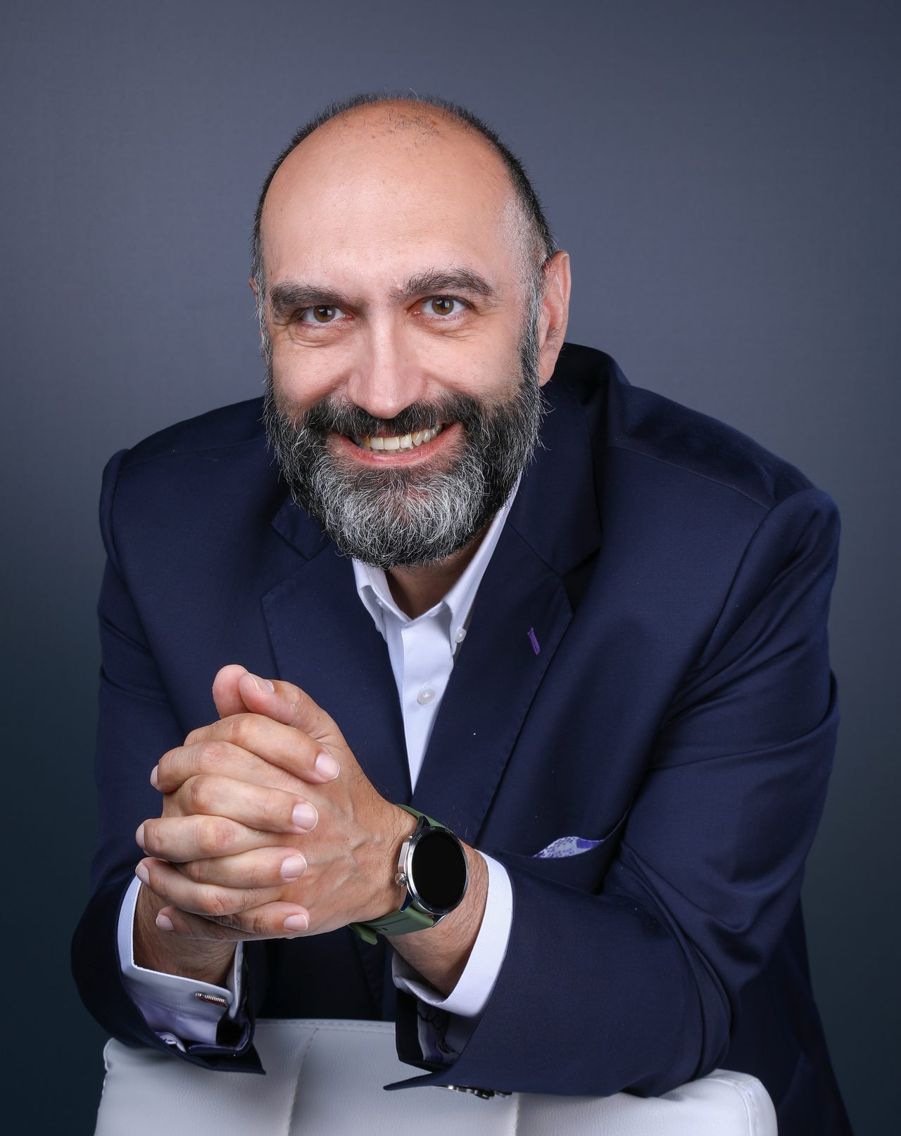 Malek Mroueh smiling in a navy jacket, with his hands clasped
